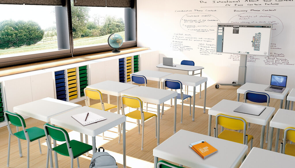 Un aula luminosa con mobiliario escolar moderno: pupitres blancos y sillas de colores, algunas con ordenadores portátiles, cuadernos y una mochila. Grandes ventanales llenan el espacio de luz solar; cerca de la pared del fondo hay una pizarra blanca y un globo terráqueo cubiertos de notas.